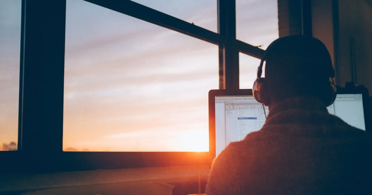 A creative with headphones working at a computer as the sun sets
